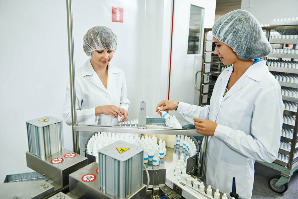Two woman working at a machine with bottles .